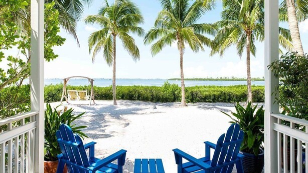 A covered outdoor area with a view of the beach, palm trees, and a swing set. - Work From Here at Parrot Key Hotel & Villas (Key West)