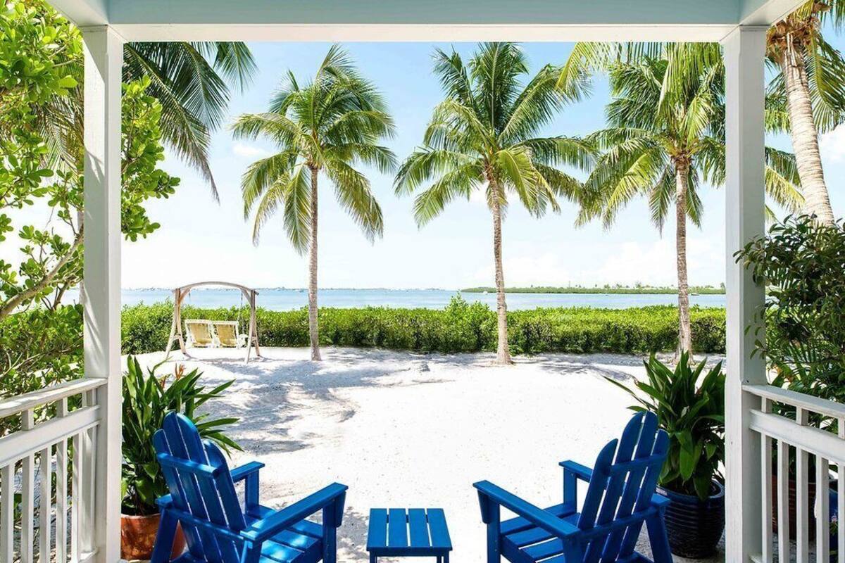 A covered outdoor area with a view of the beach, palm trees, and a swing set.