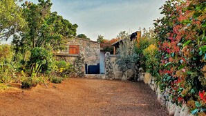 A rustic stone building with a wooden door and a small window, surrounded by lush greenery and a gravel path. - Santa-Giulia beach&Bergerie&U Caseddu (Porto-Vecchio)