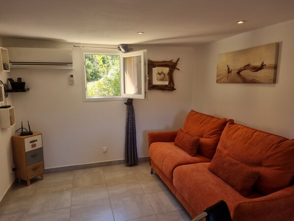 A living room with a sofa, a window, a wall-mounted artwork, and a small cabinet. - Santa-Giulia Beach & Bergerie & U Caseddu (Porto-Vecchio)