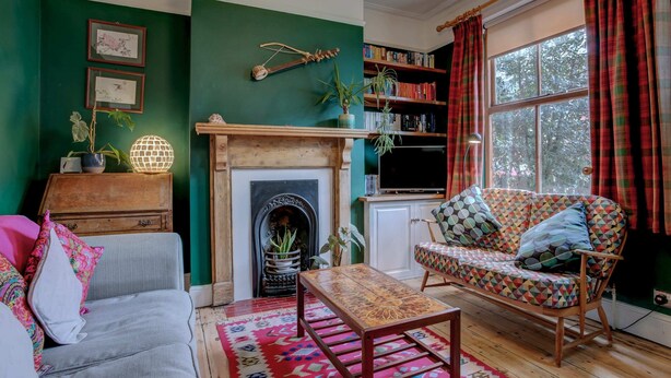Een gezellige woonkamer met een open haard, een bank, een vloerkleed met patroon en een boekenkast.