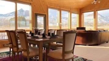 Un intérieur en bois comprenant une table et des chaises, un canapé et de grandes fenêtres donnant sur une vue sur les montagnes.