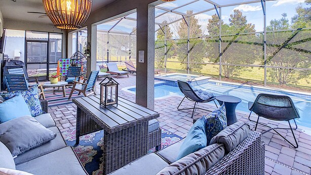 A sunlit patio with wicker furniture, a pool, and large windows offering a view of the outdoors.