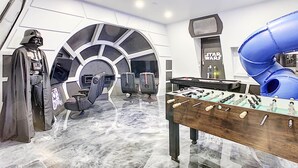 A room with a Star Wars theme, including a Darth Vader statue, a large screen, and a blue slide.