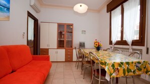 A dining area with a table set for four, a sofa, and a cabinet with glass doors. - Spacious flat 50m from the beach (Rosolina Mare)