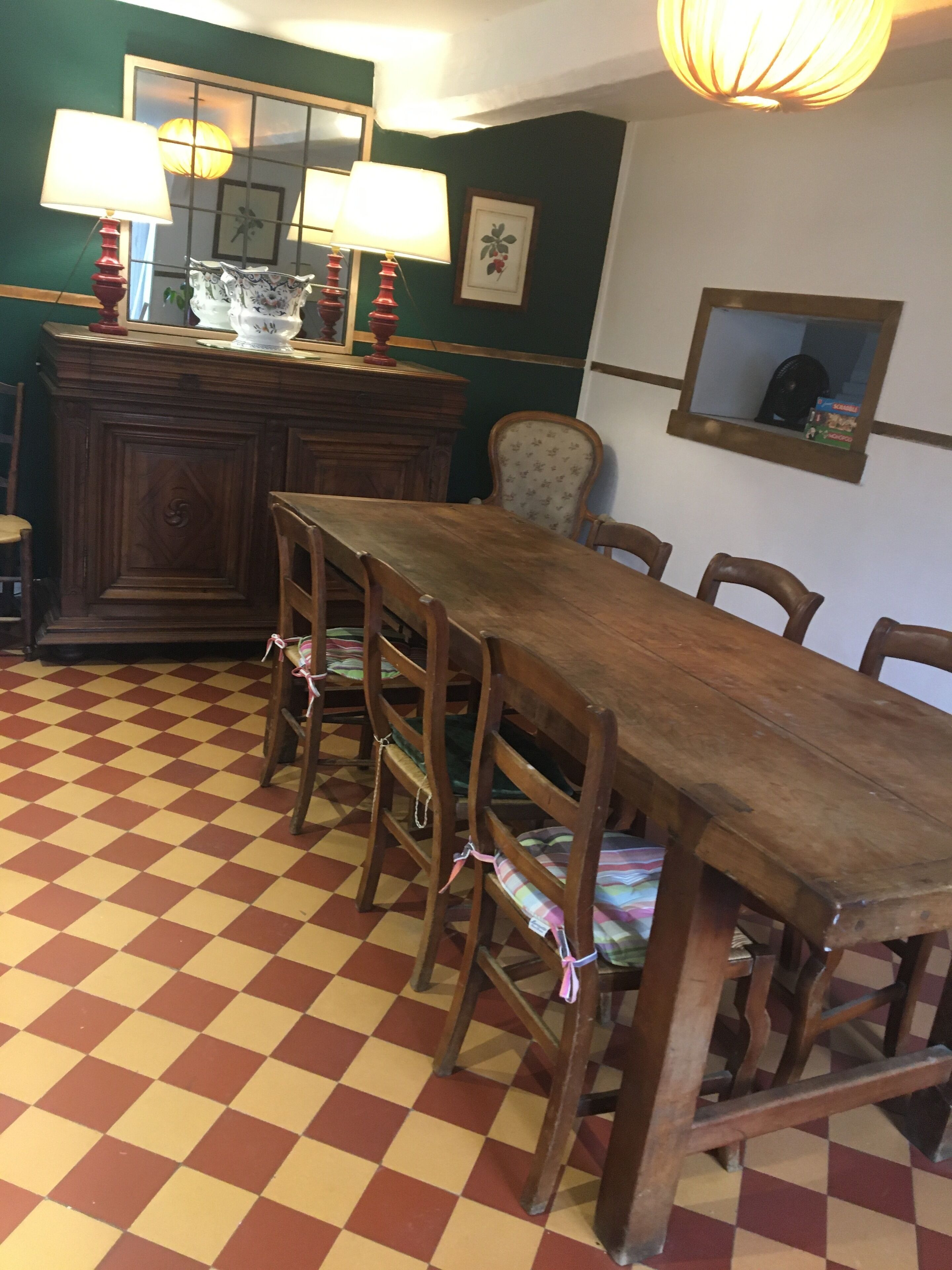 Zona pranzo con tavolo e sedie in legno, pavimento a scacchi e parete verde con specchio e quadro incorniciato.