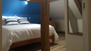 A bedroom with a bed, a chair, and a wooden ceiling beam.