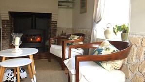 A cozy living room with a fireplace, wooden chairs, a small table, and a potted plant.