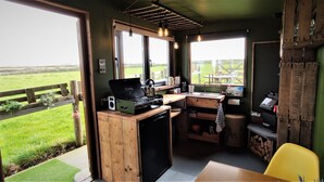 A compact kitchen with a stove, sink, and wooden cabinets, overlooking a grassy field. - The Bolt Hole (Saint Merryn)