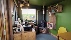 A cozy room with a large window, a wood-burning stove, a radio, and a wooden table. - The Bolt Hole (Saint Merryn)