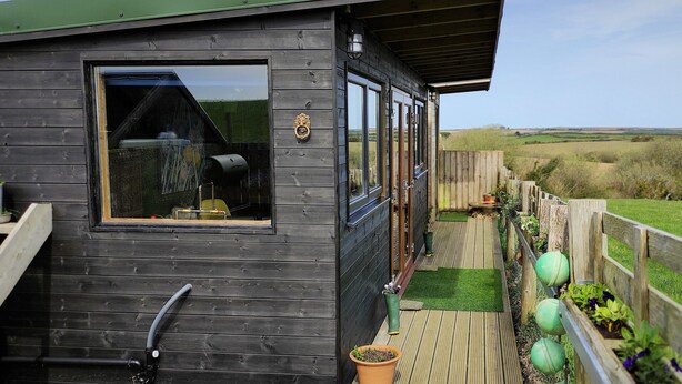 A wooden cabin with a large window, a deck, and a view of the countryside. - The Bolt Hole (Saint Merryn)