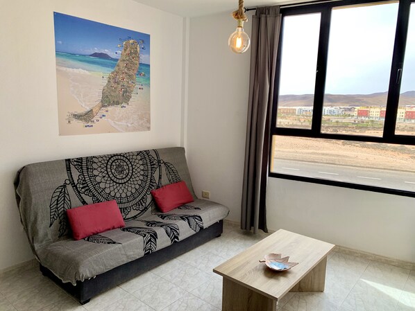 Ein Wohnzimmer mit einer Couch, einem Couchtisch, einer Karte an der Wand und Blick durch ein Fenster.