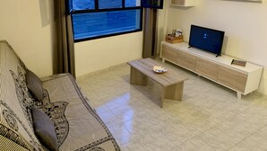 Ett modernt vardagsrum med ett stort fönster, en soffa, ett soffbord, en tv och ett träskåp.