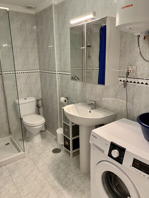 Ein modernes Badezimmer mit einer Duschkabine, einer Toilette, einem Waschbecken und einer Waschmaschine.