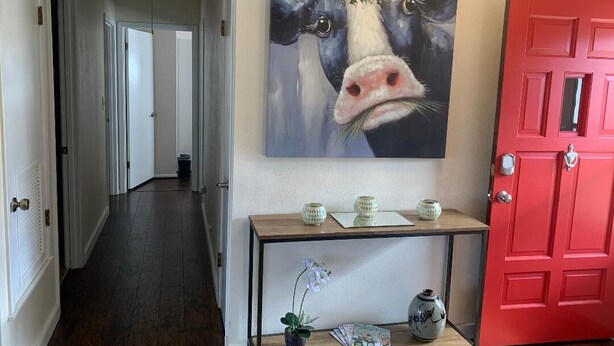 A hallway with a red door, a painting of a cow, and a console table with decorative items. - " BLUE SKYLARK"  is two blocks from main and one mile from Historic downtown.  (Fredericksburg)