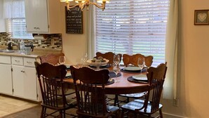 A dining area with a round table set for six, surrounded by wooden chairs. A chandelier hangs above, and a window with blinds is visible in the background. - " BLUE SKYLARK"  is two blocks from main and one mile from Historic downtown.  (Fredericksburg)