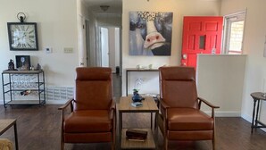 A living room with two brown leather chairs, a wooden coffee table, a patterned rug, a clock on the wall, and a red door in the background. - " BLUE SKYLARK"  is two blocks from main and one mile from Historic downtown.  (Fredericksburg)