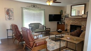 A living room with a fireplace, a ceiling fan, a television, and a dining area with chairs and a table. - " BLUE SKYLARK"  is two blocks from main and one mile from Historic downtown.  (Fredericksburg)