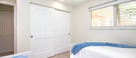 A bedroom with two beds, a window with blinds, a ceiling fan, and a white door.