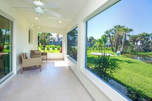 A modern room with a large window, a ceiling fan, and a view of a well-maintained garden with a pond.