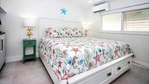 Une chambre à coucher comprenant un lit, une table de chevet, un ventilateur de plafond et une fenêtre avec des stores.
