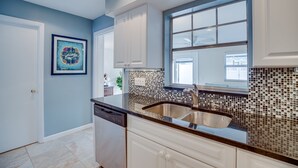 A kitchen with white cabinets, a stainless steel sink, and a backsplash with mosaic tiles. - Central Beach 2 BR under the oaks on Cardinal Drive; 2 min, walk to beach (Vero Beach)