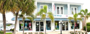 A two-story building with a blue and white facade, a sign reading "Beach Shop," and palm trees in front.