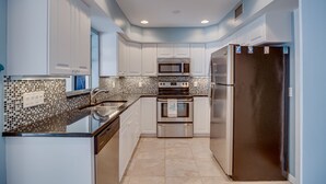 A modern kitchen with white cabinets, a stainless steel refrigerator, a microwave, and an oven. - Central Beach 2 BR under the oaks on Cardinal Drive; 2 min, walk to beach (Vero Beach)