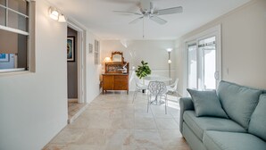 A modern living room with a grey sofa, a dining table with chairs, a ceiling fan, and a large window. - Central Beach 2 BR under the oaks on Cardinal Drive; 2 min, walk to beach (Vero Beach)