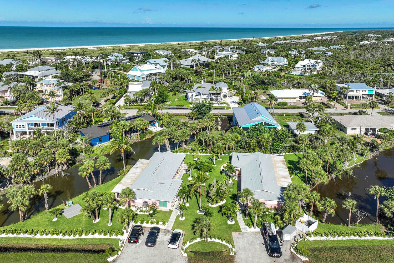 An aerial view of a residential area with houses, palm trees, and a beach in the background.