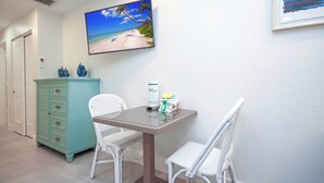 A room with a television displaying a beach scene, a small table with cleaning supplies, and a white chair. - West End Paradise Unit Coral 4 - One bedroom efficiency suite (Sanibel)