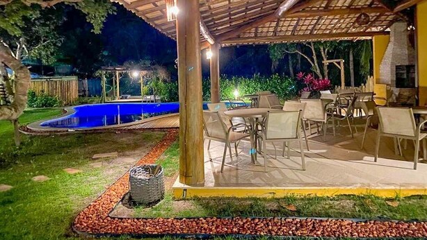 An outdoor patio with a pergola, seating area, and a swimming pool at night. - MSP01 Apt 3 Quartos Pé na Areia (Cairu)