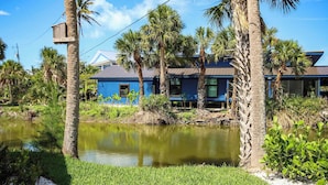 Een blauw gebouw met een vijver ervoor, omringd door palmbomen en begroeiing.