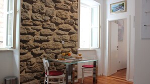 A dining area with a stone wall, a glass table, and two white chairs with red cushions.