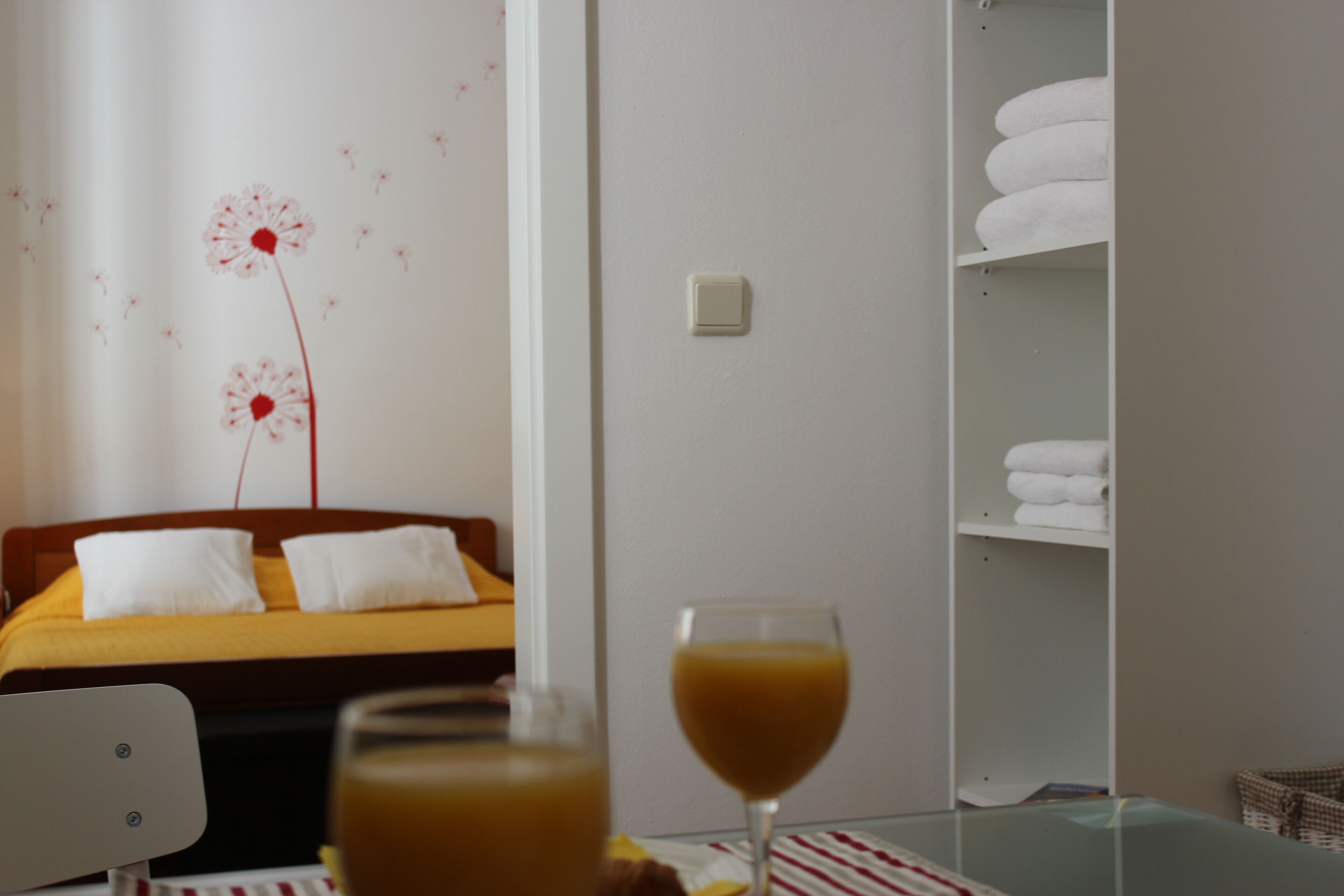 A hotel room with a bed, a bedside table with a glass of orange juice, and a wardrobe with folded towels.