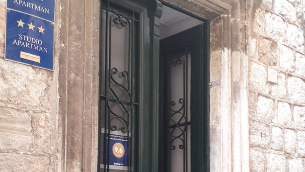 A black door with a metal gate, a blue sign with stars and text, and a potted plant on the ground.