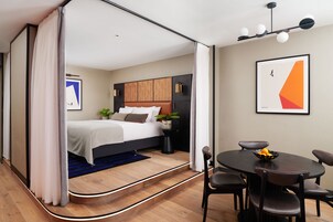 Una habitación de hotel moderna con cama, una mesa de comedor con sillas y una mesita auxiliar.