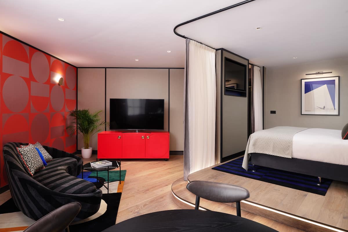 Una habitación de hotel moderna con televisión de pantalla plana, una cama, un sofá, un armario rojo y una planta en maceta.