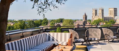 A rooftop terrace with a striped sofa, wicker chairs, and a wooden table.