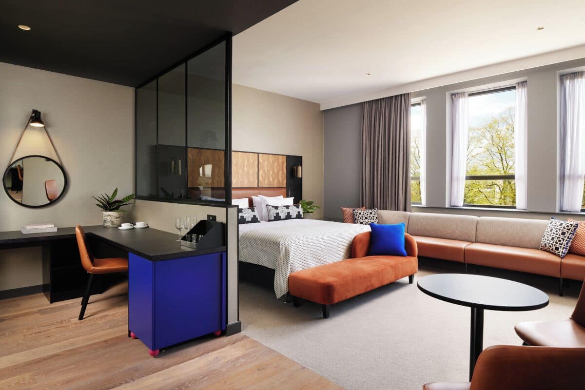 Una habitación de hotel moderna con escritorio, cama, sofá y una mesa redonda.