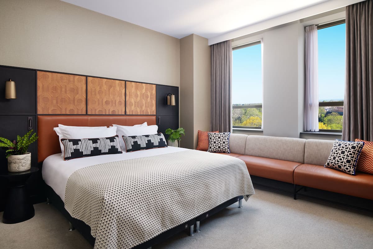 Una habitación de hotel moderna con una cama grande, un sofá, vistas al exterior y un cabecero decorativo.