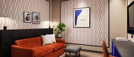 Una habitación de hotel moderna con sofá, una mesita, una silla y obras de arte enmarcadas en las paredes.
