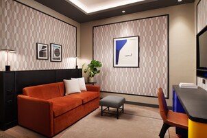 Una habitación de hotel moderna con sofá, una mesita, una silla y obras de arte enmarcadas en las paredes.