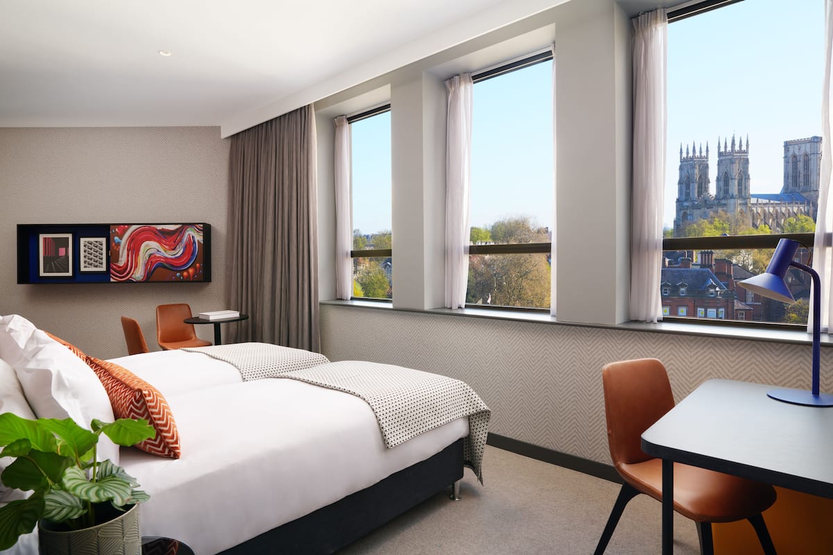 Habitación de hotel con una cama grande, un escritorio, una silla y vistas a una catedral desde la ventana.