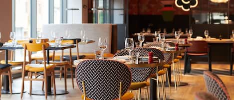 A restaurant interior with round tables, yellow chairs, and hanging pendant lights.