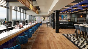 A modern bar area with a long counter, blue patterned chairs, and a view of the city. - Malmaison York (York)