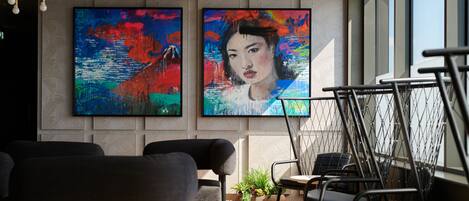 A modern interior with two large abstract paintings on the wall, a seating area with sofas and tables, and a view of the outside through large windows.