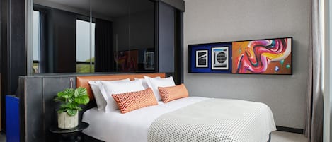 Una camera d'albergo moderna con un letto grande, un tavolino con una pianta, un ampio specchio e arte astratta appesa al muro.