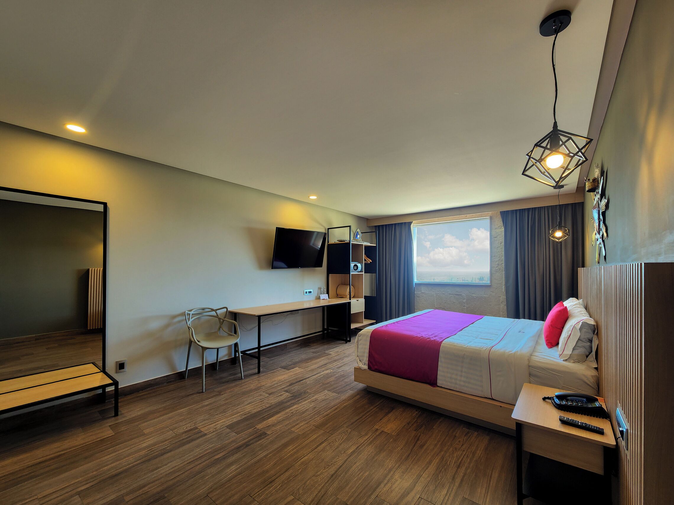 A modern hotel room with a bed, desk, chair, and a TV.