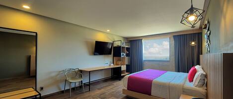 A modern hotel room with a bed, desk, chair, and a TV.